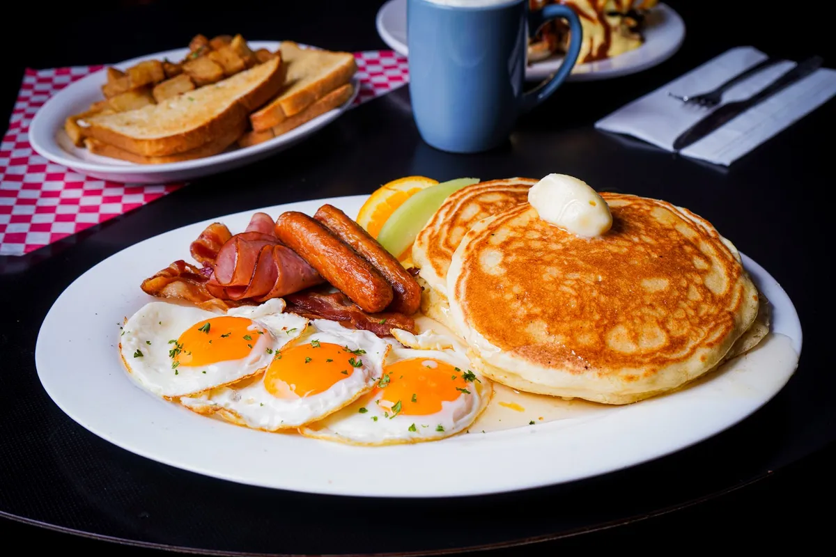 Large breakfast plate with pancakes, eggs, bacon, and sausage