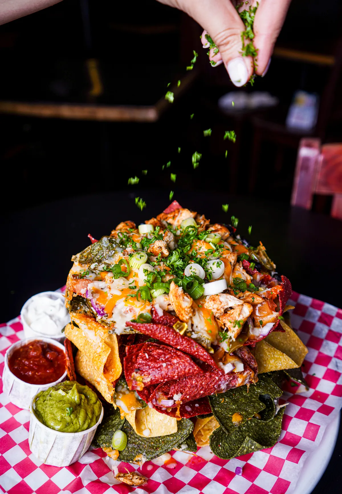 Large plate of loaded nachos with dips and a hand sprinkling herbs